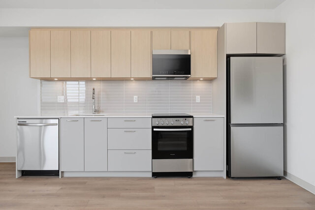 Straight-on kitchen with light oak upper cabinets, grey lower cabinets, under-cabinet lighting, a tile backsplash and a stain