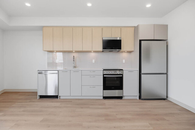 Kitchen wall with light oak cabinets over grey lowers, a tile backsplash and stainless appliances. - 619-1529 Oxford Street, North Vancouver