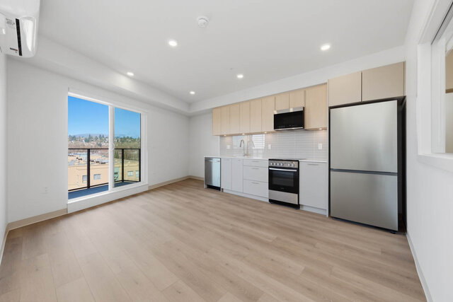 Open living area with a sliding glass door to the balcony, a wall air conditioner and the kitchen along the far wall.