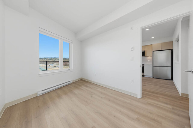 Second bedroom with a big window, its door opening toward the kitchen and stainless fridge. - 619-1529 Oxford Street, North Vancouver