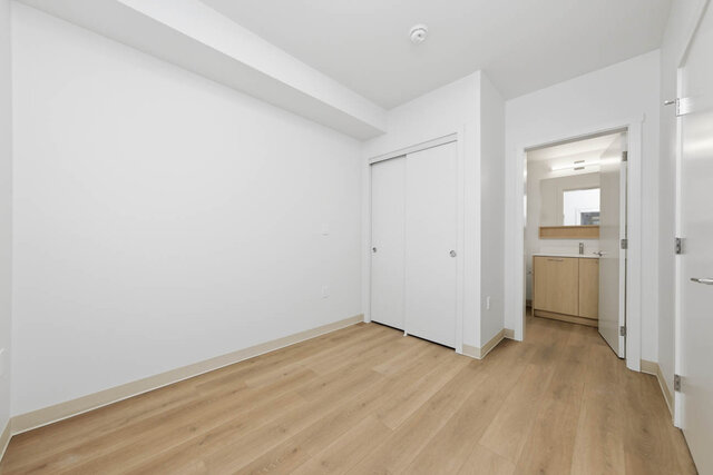 Empty primary bedroom with a sliding closet and an open door to its ensuite with a light wood vanity. - 424-1529 Oxford Street, North Vancouver