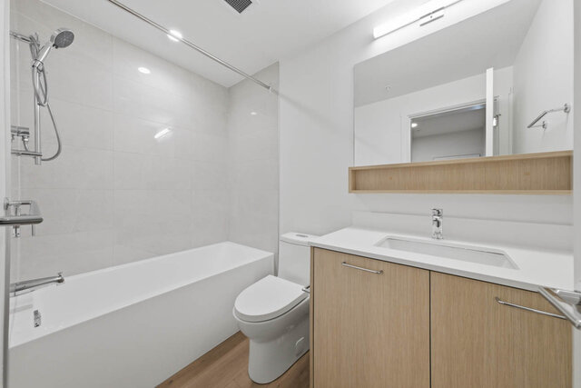 Full bathroom with a tub and shower, a tile surround and a light wood vanity with a quartz counter under a mirror and open sh