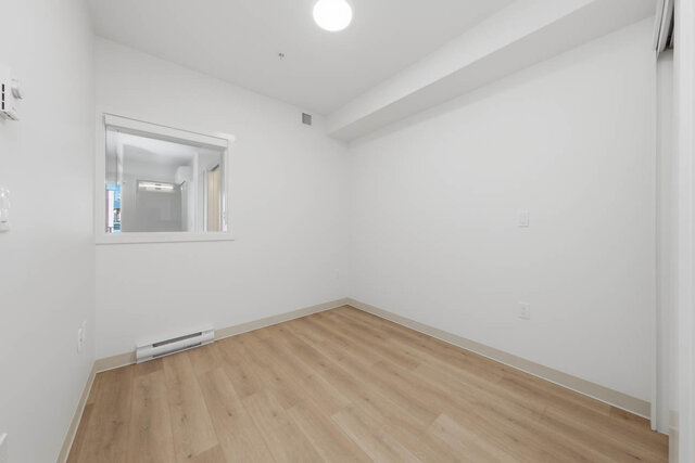 Empty primary bedroom with a sliding closet and an interior window to the living area. - 424-1529 Oxford Street, North Vancouver