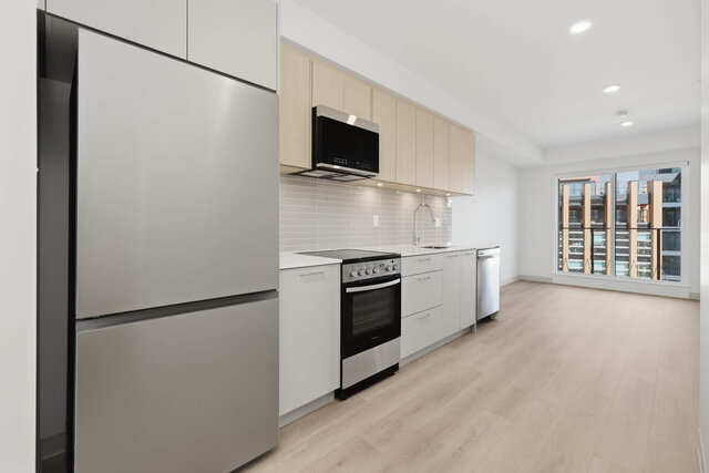 Galley kitchen with a stainless fridge, range, microwave and dishwasher under light oak upper cabinets, running to the slidin