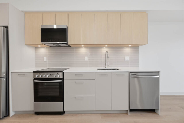 Straight-on kitchen with light oak upper cabinets, grey lower cabinets, a quartz counter, under-cabinet lighting, a stainless