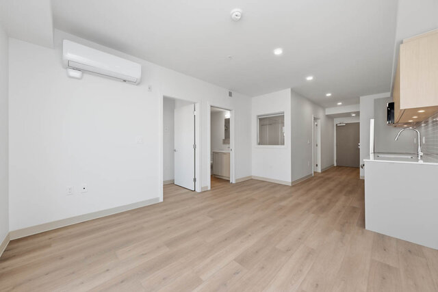 Empty living room with a wall air conditioner and side-by-side doors to the second bedroom and a bathroom. - 424-1529 Oxford Street, North Vancouver