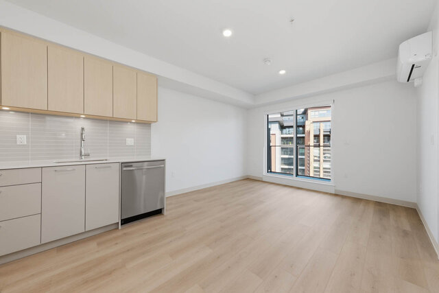 Open living and dining area beside the kitchen, with a sliding glass door to the balcony and a wall air conditioner.