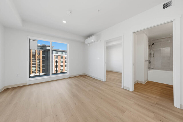 Living room with a sliding glass door to the balcony, a wall air conditioner, and doors to the second bedroom and a bathroom 
