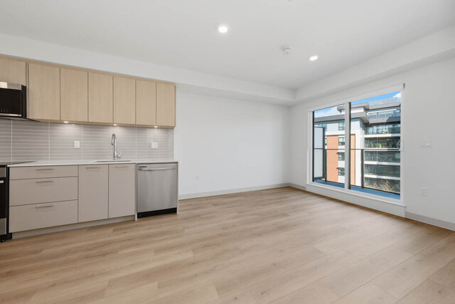 Open living and dining area with the kitchen on the left and a wide sliding glass door to the balcony. - 424-1529 Oxford Street, North Vancouver