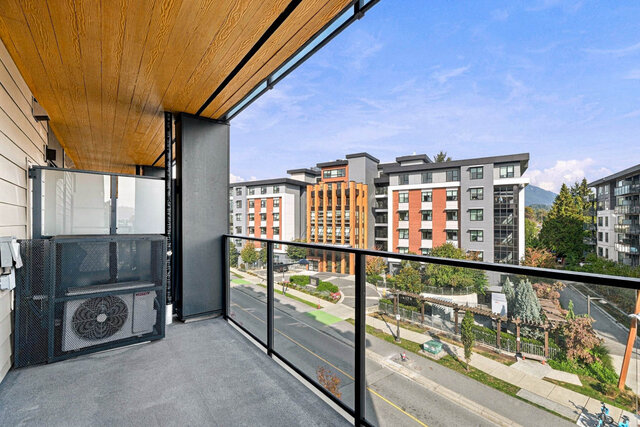 Covered balcony with a wood ceiling and glass railing, facing the neighbouring buildings with a mountain glimpse between them