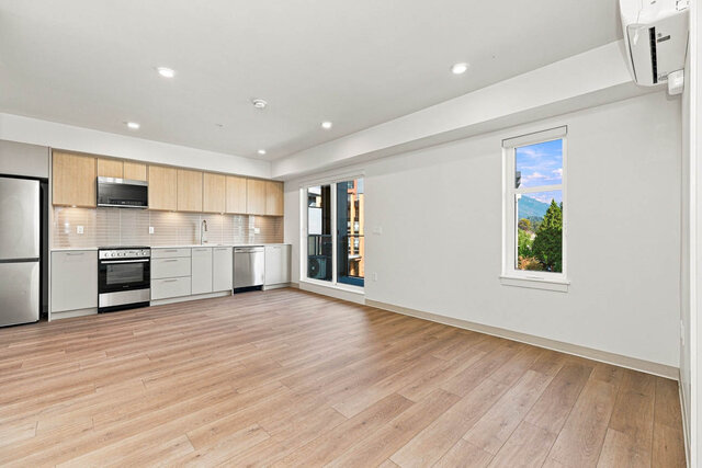Empty open living and dining room with the kitchen along one wall, a sliding glass door to the balcony, a second window with 