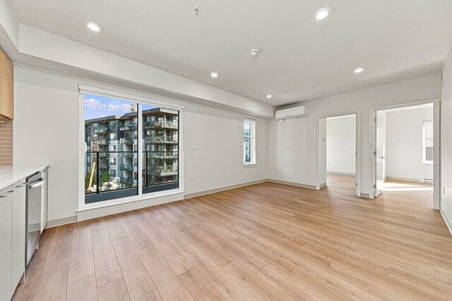 Open living room with a sliding glass door to the balcony, a second window, a wall air conditioner and doors to both bedrooms