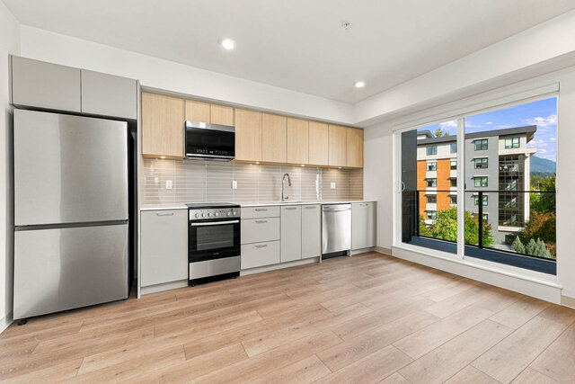 Kitchen with a stainless fridge, range, microwave and dishwasher, light oak upper cabinets and under-cabinet lighting, beside