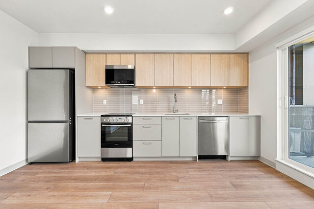 Straight-on kitchen with a stainless fridge, range, microwave and dishwasher, light oak upper cabinets, grey lower cabinets, 