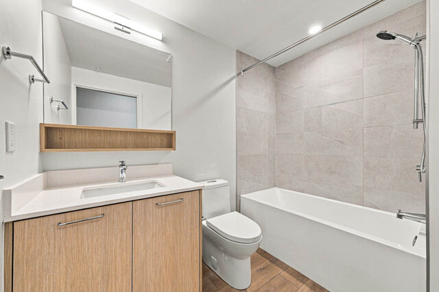 Second full bathroom with a tub and shower, a tile surround and a light wood vanity with a quartz counter. - 405-1529 Oxford Street, North Vancouver