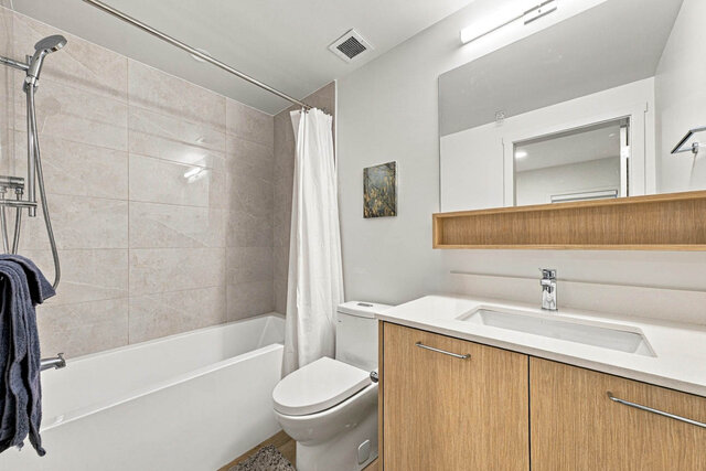 Full bathroom with a tub and shower, a tile surround, a light wood vanity with a quartz counter and a mirror over an open she