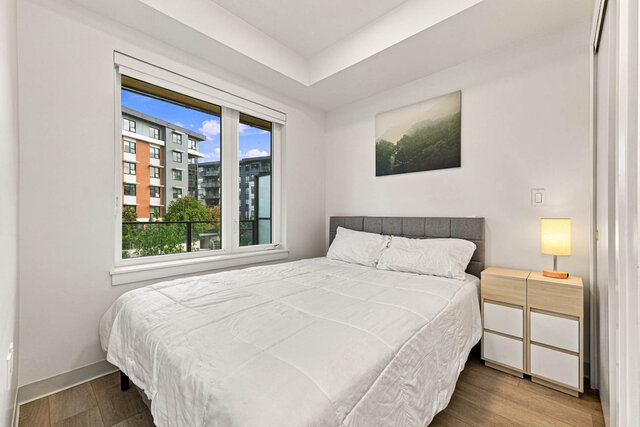Second bedroom with a queen bed, a grey upholstered headboard, nightstands with a lamp, a big window and a closet on the righ