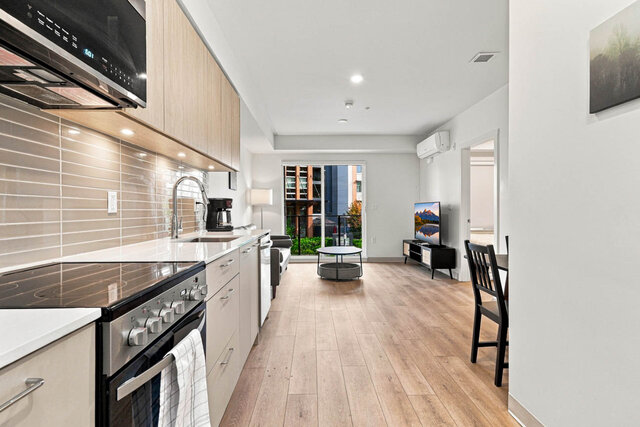 Kitchen counter running straight to the living room, with a stainless range and microwave, the dining table on the right and 