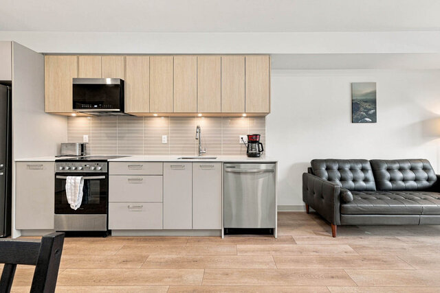 Straight-on kitchen with light oak upper cabinets, grey lower cabinets, a quartz counter, under-cabinet lighting, a stainless