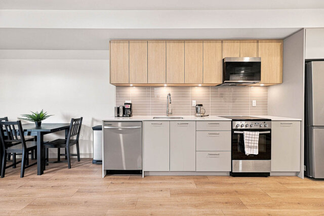 Straight-on galley kitchen with light oak upper cabinets, grey lower cabinets, under-cabinet lighting, stainless appliances, 