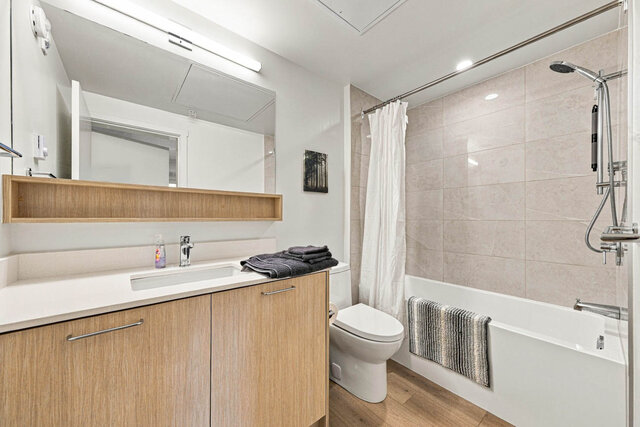 Full bathroom with a tub and shower, a tile surround and a light wood vanity with a quartz counter under a wide mirror and op