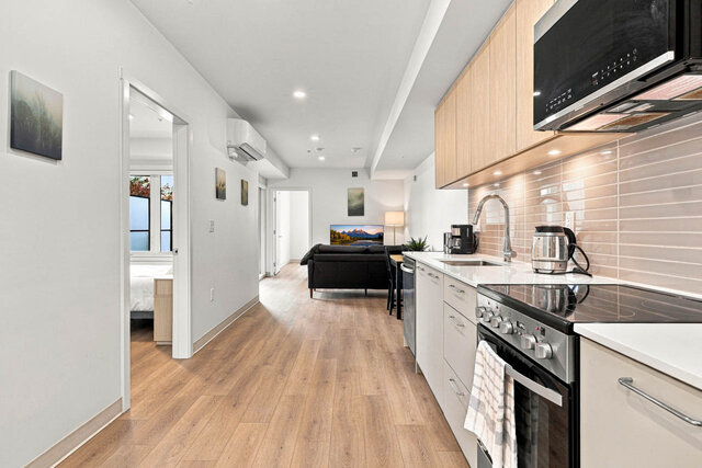Kitchen counter with a stainless range and microwave under light oak cabinets, looking down the suite to the living area, wit