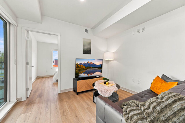 Living room with a leather sofa, a TV on a media console, a coffee table and floor lamp, beside the sliding glass door and an