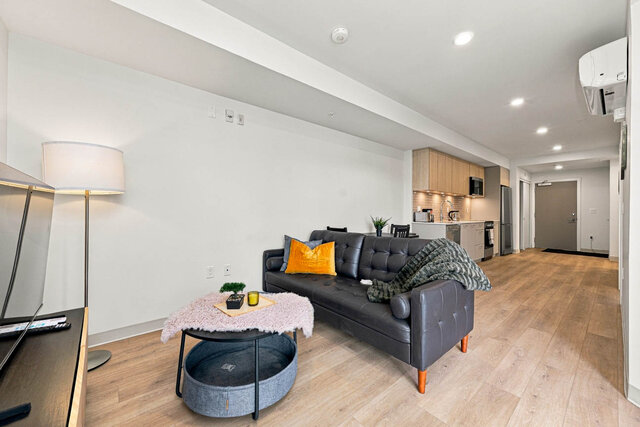 Long open living area with a leather sofa and coffee table, looking back past the kitchen to the front door under a wall air 