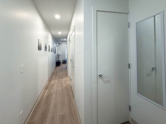 Long hallway lined with art, leading from the front door past the bathroom to the living room. - 101-1529 Oxford Street, North Vancouver