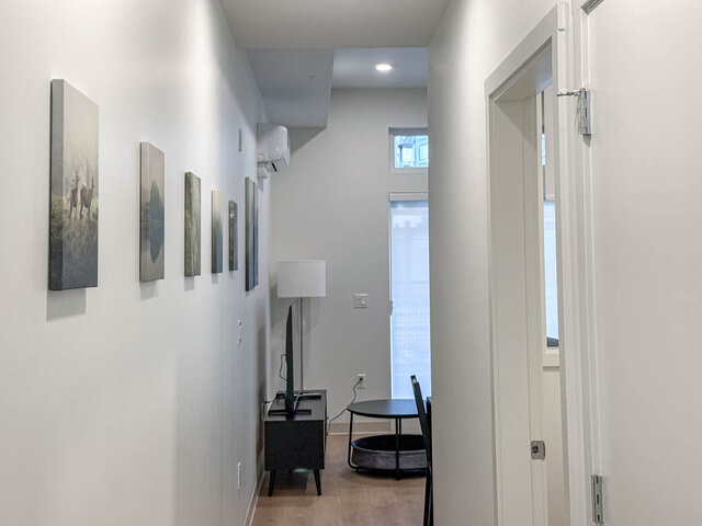 Hallway with a row of art leading to the living room and its tall window. - 101-1529 Oxford Street, North Vancouver