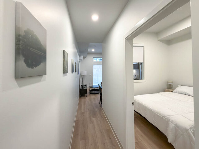 Hallway past the bedroom door, with the queen bed inside and an interior window. - 101-1529 Oxford Street, North Vancouver