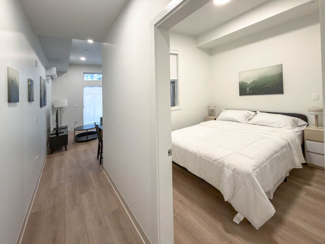 Bedroom with a queen bed, two nightstands with lamps and an interior window that borrows light from the living room.