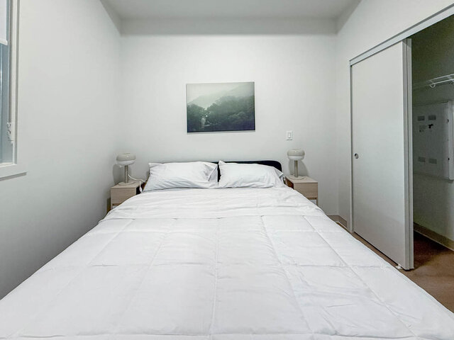 Queen bed between two nightstands with lamps, beside a closet with sliding doors. - 101-1529 Oxford Street, North Vancouver