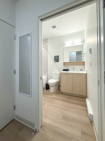 Bathroom seen from the doorway, with a wood vanity, lit mirror and tub. - 101-1529 Oxford Street, North Vancouver
