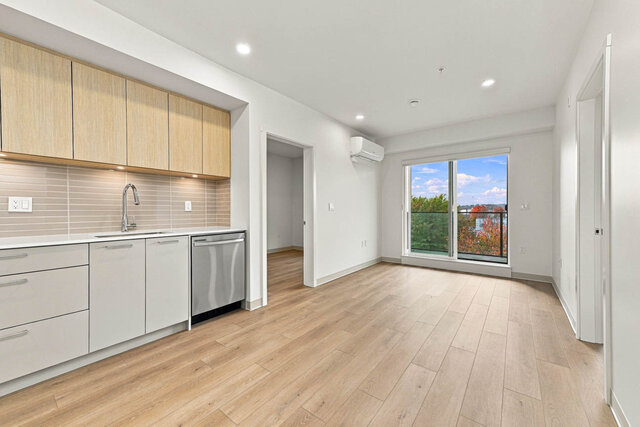 Living and dining space beside the kitchen, with a sliding door to the balcony and bedroom doors on either side.
