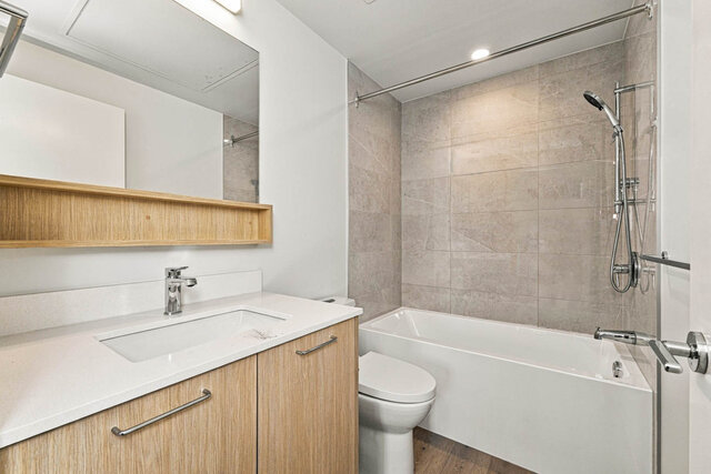 Second full bathroom with a tub and shower, tile surround, a wood vanity with a quartz counter and a mirror with an open shel