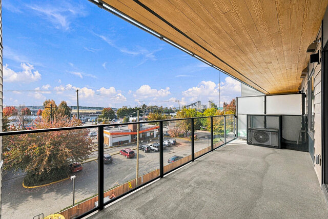 Long covered balcony with a wood ceiling and glass railing, looking out over autumn trees and the neighbourhood.