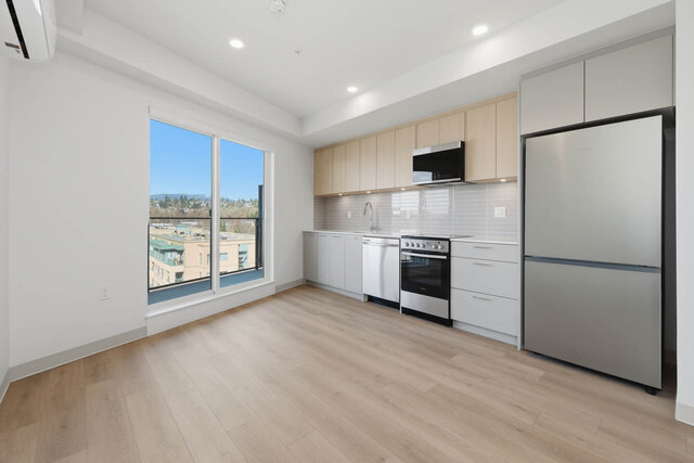 Kitchen along one wall with light oak upper cabinets, quartz counters, a tile backsplash and stainless appliances, beside the