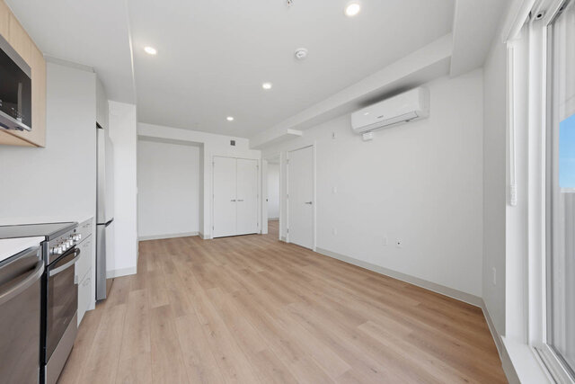 Living and dining area looking back past the kitchen toward a double closet and the bedroom doors, with an air conditioner on