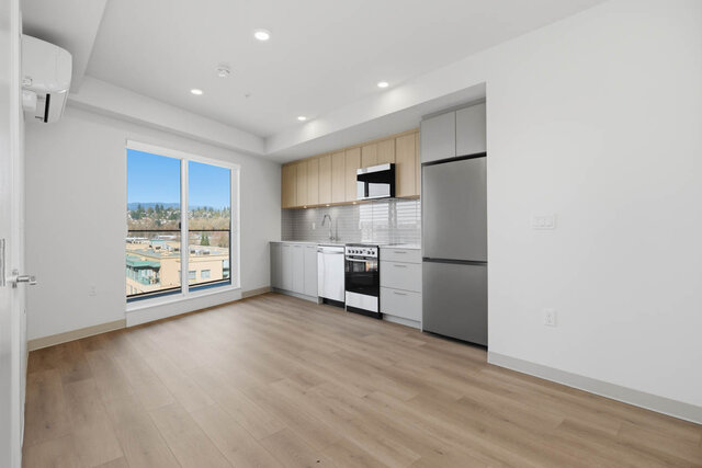 Empty living area with the kitchen along the back wall and a sliding door to the balcony. - 518-1529 Oxford Street, North Vancouver