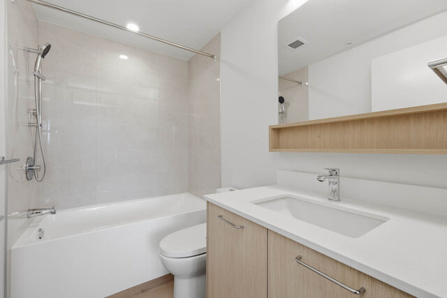 Full bathroom with a tub and shower, tile surround, a wood vanity with a quartz counter and a mirror with an open shelf.