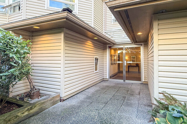 Covered front entrance of Cedarcrest with glass double doors into the lobby, an intercom panel and planted beds either side.