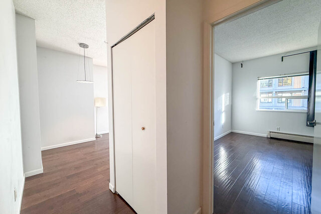Hallway with a closet between the living room on the left and the bedroom with a window on the right, hardwood floors.