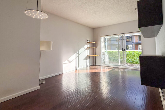 Sunny living room with a pendant light, open shelving and a sliding glass door out to the balcony, hardwood floors.