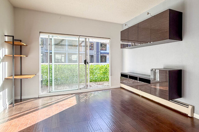 Living room with a wide sliding glass door to the balcony, wall-mounted cabinets and open shelving, hardwood floors in sunlig