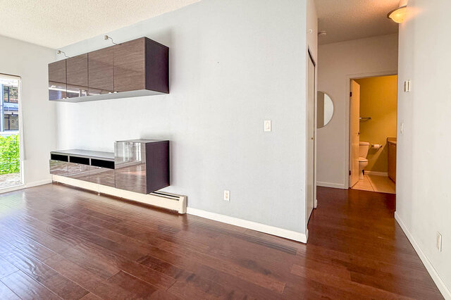 Living room wall with wall-mounted cabinets, looking down the hall to the bathroom, hardwood floors. - 304-827 West 16th Street, North Vancouver
