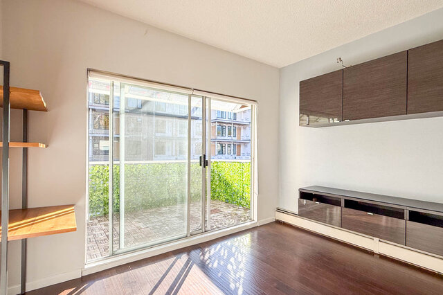 Living room by the sliding glass door, with the balcony and its leafy privacy screen just outside, hardwood floors.