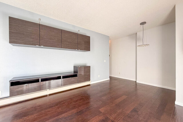 Long living room with wall-mounted cabinets and a pendant light over the dining end, hardwood floors. - 304-827 West 16th Street, North Vancouver