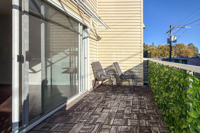 Generous private balcony with wood deck tiles, a leafy privacy screen along the railing and two chairs in the sun.