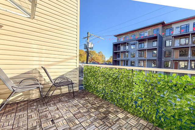 Private balcony with wood deck tiles, two chairs and a leafy privacy screen, under a blue sky. - 304-827 West 16th Street, North Vancouver